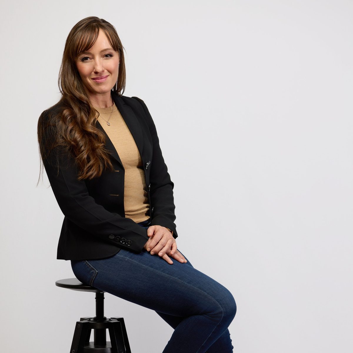 Jessica Billingsley seated on a stool in a black blazer